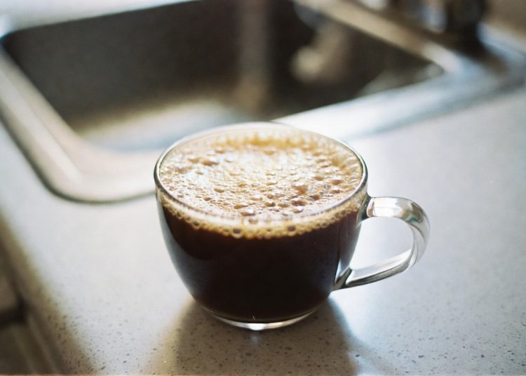 Glass cup of fresh black coffee on kitchen counter, clever coffee tip to pour liquid creamer into the cup before adding hot coffee
