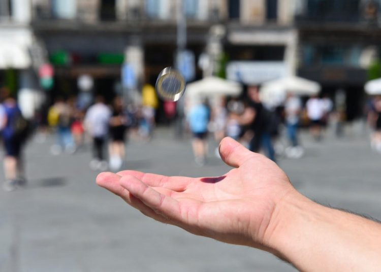 Hand flipping a silver coin in a busy public square, decision-making technique using coin toss to clarify what you really want