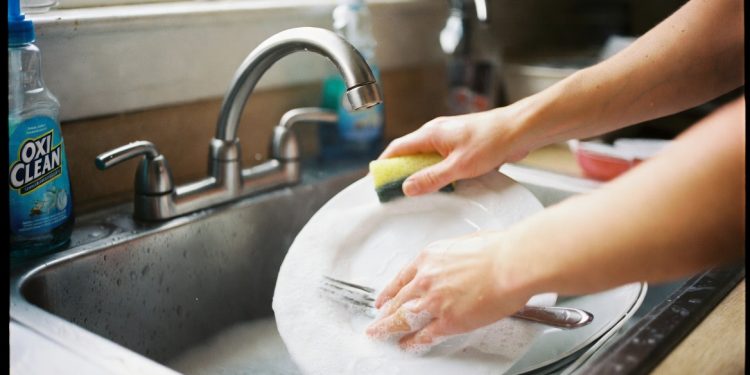 Hands washing dishes in a sink filled with soapy water and OxiClean, effective kitchen cleaning hack using dish detergent and OxiClean for easier dishwashing
