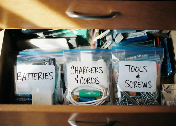 Neatly organized junk drawer with labeled Ziploc bags for batteries, chargers and cords, tools and screws, smart decluttering and organization hack