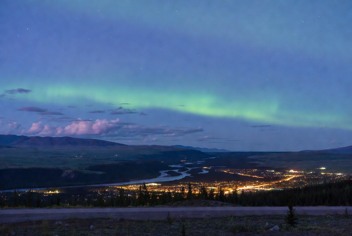 Northern Lights aurora borealis glowing over Whitehorse Yukon Canada at night with city lights and wilderness