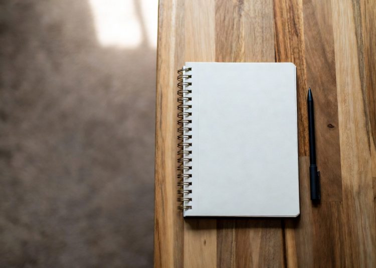Spiral notebook and black pen placed on wooden table, productivity tip to always write down good ideas immediately instead of relying on memory