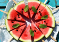 Watermelon slices on sticks arranged in a circular pattern on turquoise wooden table with mint leaves, fresh summer watermelon pops flat lay