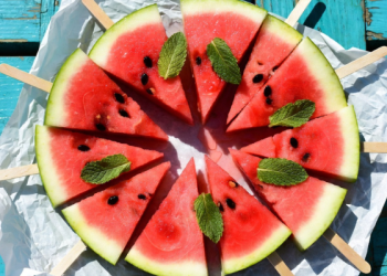 Watermelon slices on sticks arranged in a circular pattern on turquoise wooden table with mint leaves, fresh summer watermelon pops flat lay