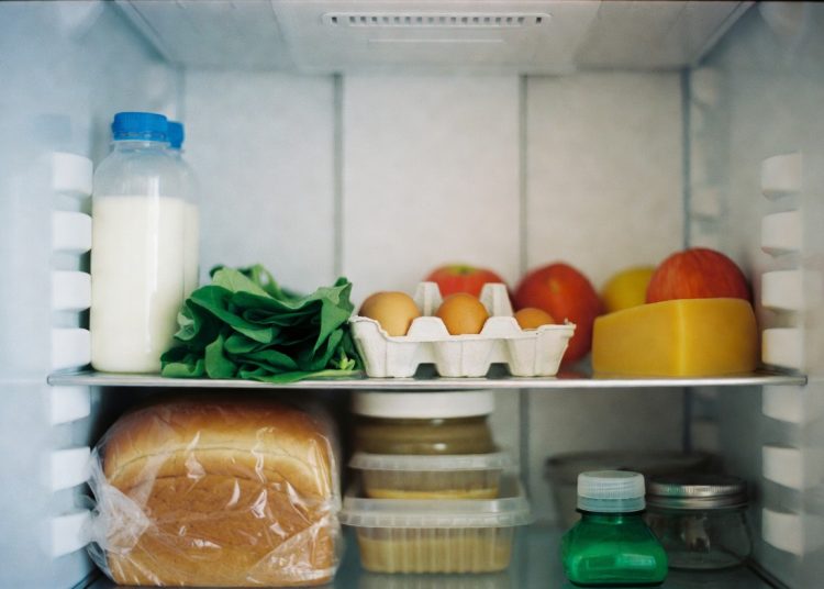 Well-stocked refrigerator interior with milk, eggs, fresh produce and cheese, smart kitchen hack to keep chalk markers on the fridge for easy labeling and organization