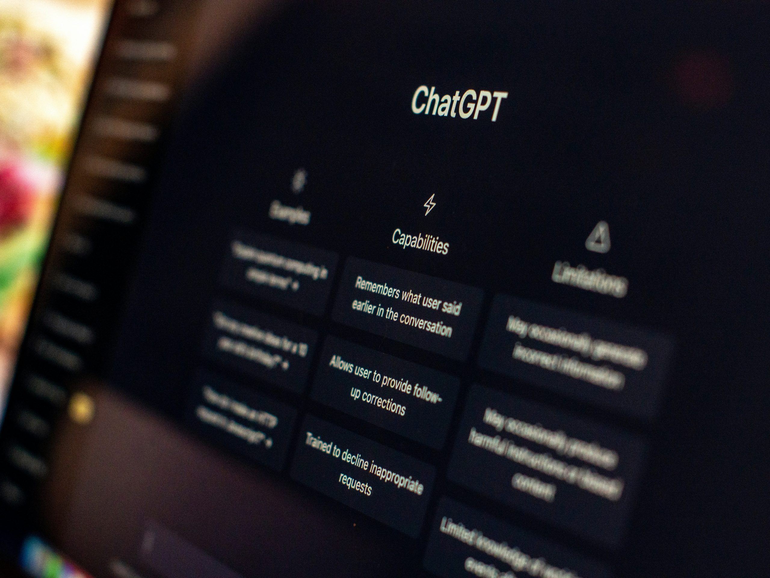 Close up photograph of the ChatGPT interface displayed on a dark computer screen with blurred background lighting, highlighting AI capabilities and conversational technology.
