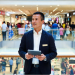 Confident retail store manager standing in a busy shopping mall, holding a tablet while overseeing operations, career growth in retail management