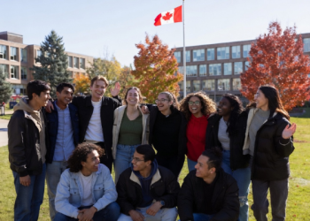 Diverse group of happy Canadian university students smiling together on a sunny autumn campus with Canadian flag waving in background