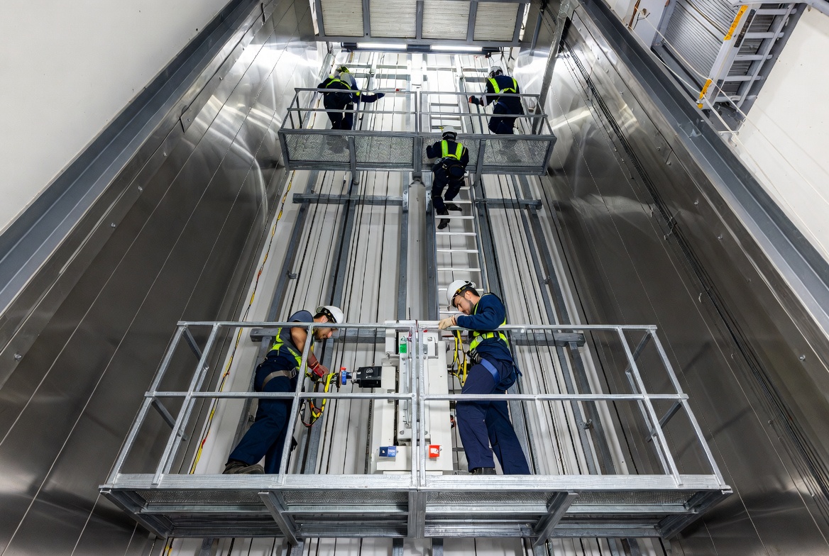 Elevator mechanics and installers in safety gear working inside a modern high-rise elevator shaft on cables and machinery