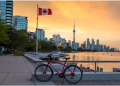Red bicycle parked on Toronto waterfront promenade with Canadian flag waving at sunset, CN Tower and city skyline in background