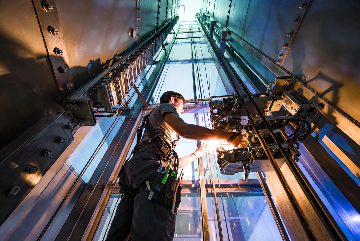 Skilled elevator mechanic performing maintenance inside a high rise elevator shaft, wearing safety harness with dramatic industrial lighting