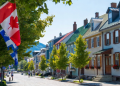 Sunny summer day on a picturesque cobblestone street in a historic Quebec town Canada colorful Victorian houses Canadian and Quebec flags waving lush green maple trees idyllic small town charm