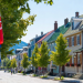 Sunny summer day on a picturesque cobblestone street in a historic Quebec town Canada colorful Victorian houses Canadian and Quebec flags waving lush green maple trees idyllic small town charm