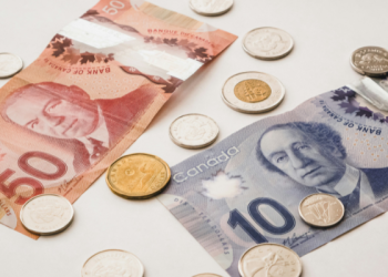 Canadian currency, featuring a red $50 bill and a purple $10 bill laid out on a light surface alongside various silver and gold Canadian coins.