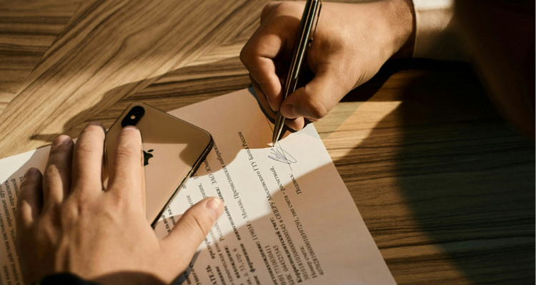 Person signing an official insurance contract or business document at a wooden table