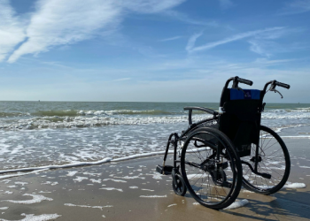Wheelchair parked on the shoreline at a sunny beach representing living with a disability
